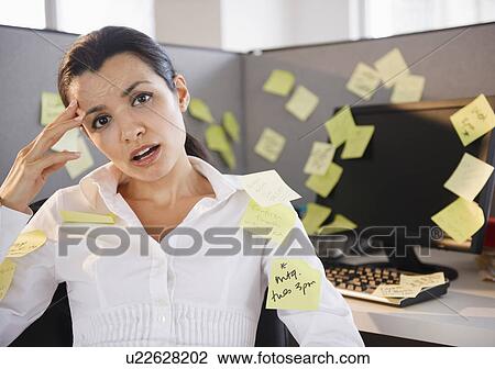 Stock Image - Businesswoman sitting at desk in office surrounded by adhesive notes. Fotosearch