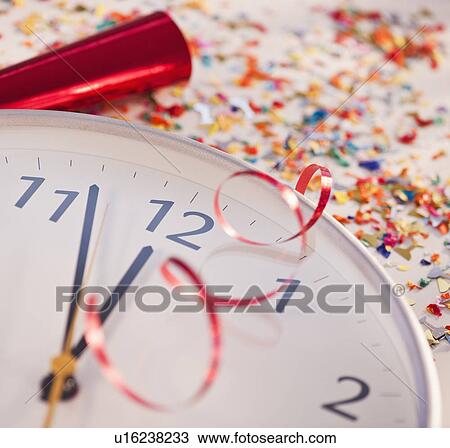 Stock Image - Confetti and ribbons on clock showing five minutes to midnight. Fotosearch