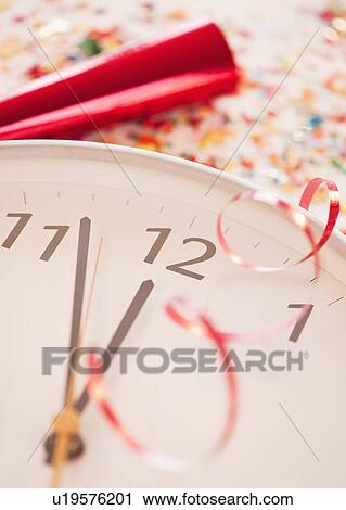 Stock Image - Confetti and ribbons on clock showing five minutes to midnight. Fotosearch