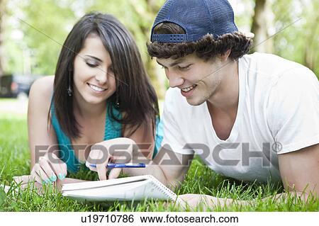 Couple lying on grass reading notes View Large Photo Image Stock Photograph - Couple lying on grass reading notes. Fotosearch