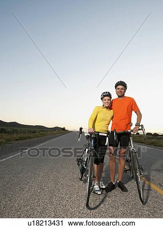 Couple of cyclists posing for portrait on empty road View Large Photo Image Stock Image - Couple of cyclists posing for portrait on empty road. Fotosearch
