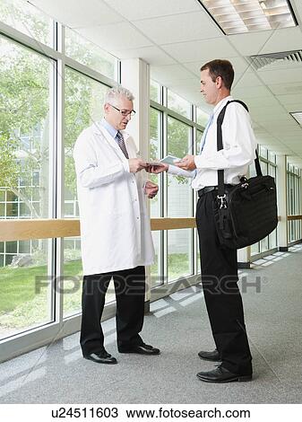 Stock Image - Doctor talking talking with pharmaceutical representative in hospital corridor. Fotosearch