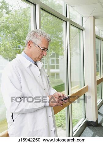 Stock Image - Doctor using mobile phone while standing in hospital corridor. Fotosearch