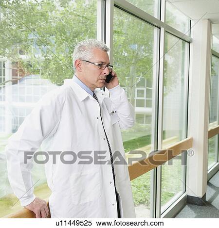 Doctor using mobile phone while standing in hospital corridor View Large Photo Image Stock Photography - Doctor using mobile phone while standing in hospital corridor. Fotosearch