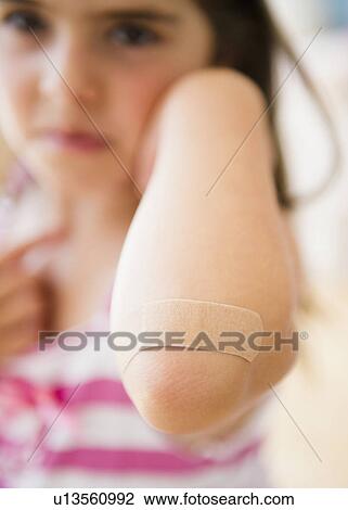 Stock Image - Girl ( 6-7) showing elbow with adhesive bandage. Fotosearch