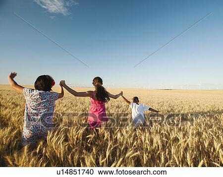 Stock Image - Girls (10-11, 12-13) and boy (8-9) walking though wheat field. Fotosearch