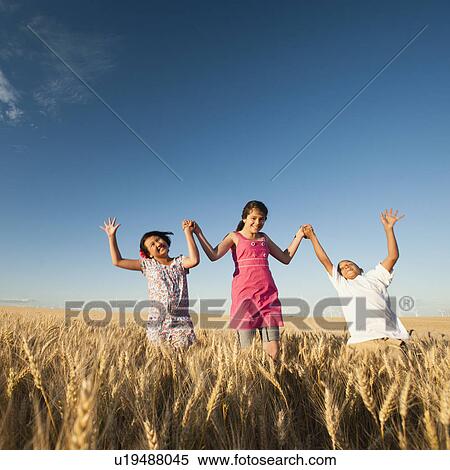 Stock Photography - Girls (10-11, 12-13) and boy (8-9) walking though wheat field. Fotosearch