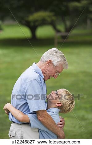 Stock Photo - Grandfather and grandson (10-11) embracing in park. Fotosearch