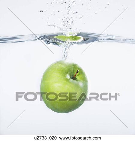 Stock Image - Green apple splashing into water, studio shot. Fotosearch