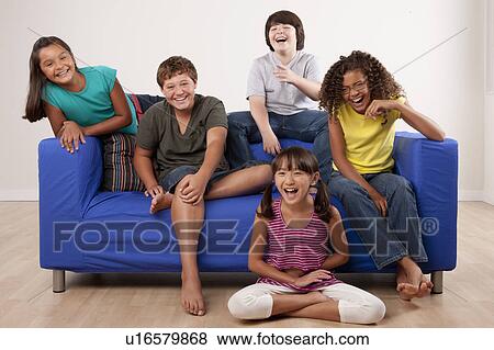 Stock Photo - Group of children (10-11, 12-13) sitting on sofa, studio shot. Fotosearch