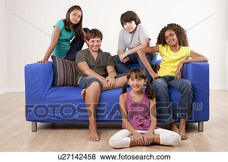 Stock Photo - Group of children (10-11, 12-13) sitting on sofa, studio shot. Fotosearch