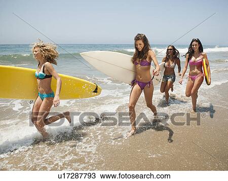 Stock Image - Group of young attractive women running into water with surfboards. Fotosearch