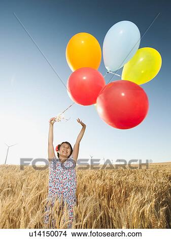 Happy girl (10-11) standing with balloons in wheat field View Large Photo Image Picture - Happy girl (10-11) standing with balloons in wheat field. Fotosearch