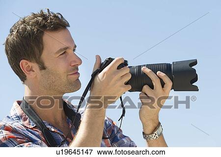 Man holding camera against blue sky View Large Photo Image Stock Photo - Man holding camera against blue sky. Fotosearch