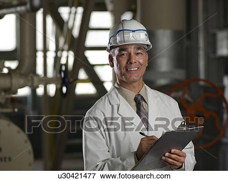 Stock Photo - Man in lab coat and hard hat holding clipboard. Fotosearch