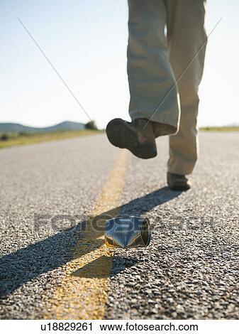 Stock Image - Man kicking tin can on otherwise empty road. Fotosearch