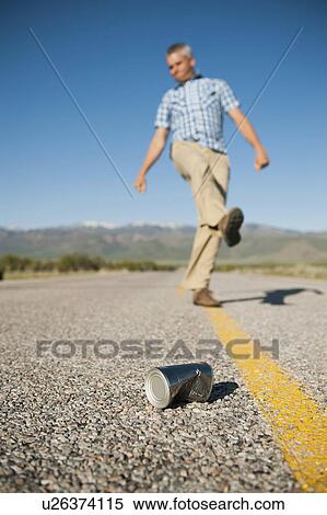 Stock Photography - Man kicking tin can on otherwise empty road. Fotosearch