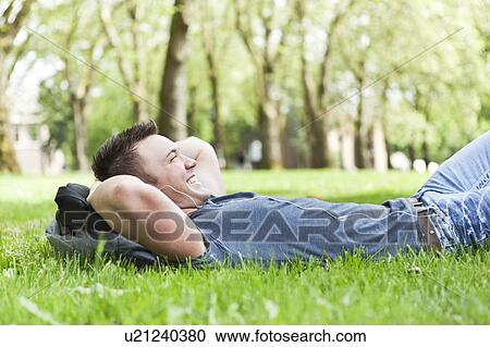 Stock Image - Man lying on grass listening to mp3 player. Fotosearch