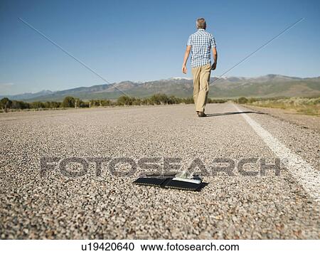 Stock Image - Man walking away leaving his wallet behind on empty road . Fotosearch