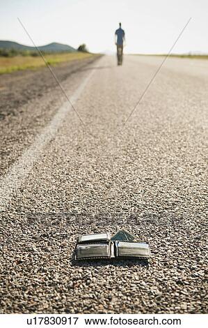 Stock Photo - Man walking away leaving his wallet behind on empty road . Fotosearch