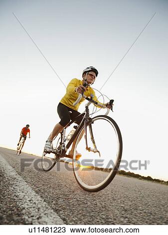 Stock Image - Mid adult couple cycling on empty road. Fotosearch