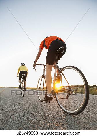 Stock Photo - Mid adult couple cycling on empty road. Fotosearch