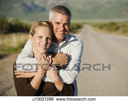 Mid adult couple embracing on empty road View Large Photo Image Stock Photograph - Mid adult couple embracing on empty road. Fotosearch