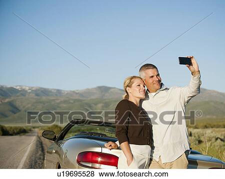 Mid adult couple photographing themselves in front of majestic mountain range View Large Photo Image Stock Photo - Mid adult couple photographing themselves in front of majestic mountain range. Fotosearch
