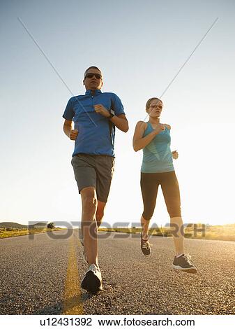 Mid adult couple running on empty road View Large Photo Image Stock Image - Mid adult couple running on empty road. Fotosearch