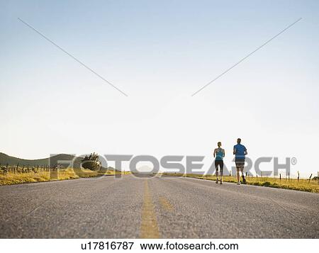 Stock Photo - Mid adult couple running on empty road. Fotosearch