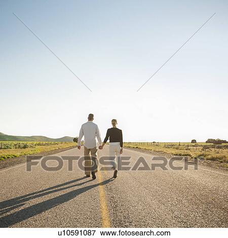 Mid adult couple walking along empty road View Large Photo Image Stock Photo - Mid adult couple walking along empty road . Fotosearch
