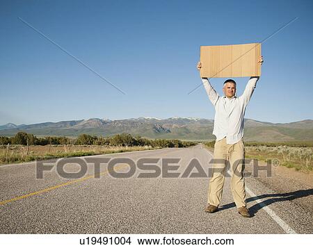 Picture - Mid-adult man hitch-hiking in barren scenery. Fotosearch