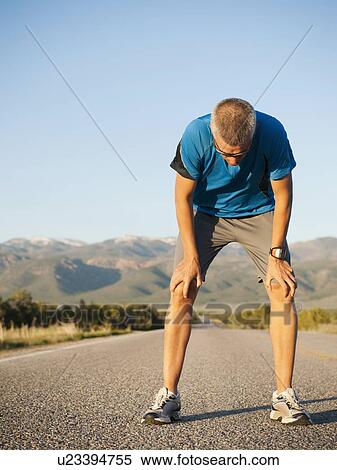 Mid adult man taking break from running on empty road View Large Photo Image Stock Photography - Mid adult man taking break from running on empty road. Fotosearch