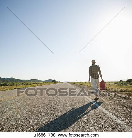 Stock Photo - Mid adult woman carrying empty canister along empty road. Fotosearch