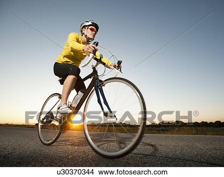 Picture - Mid adult woman cycling on empty road. Fotosearch
