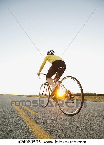 Mid adult woman cycling on empty road View Large Photo Image Stock Photography - Mid adult woman cycling on empty road. Fotosearch