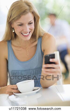 Stock Photo - Mid adult woman drinking coffee and texting. Fotosearch