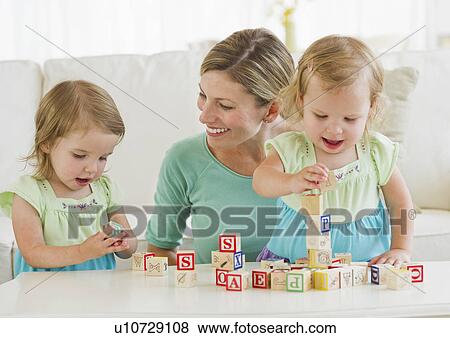 Stock Photo - Mother and daughters (2-3) playing with letter blocks. Fotosearch