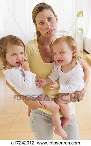 Stock Image - Mother holding crying daughters (2-3) and making facial expression. Fotosearch