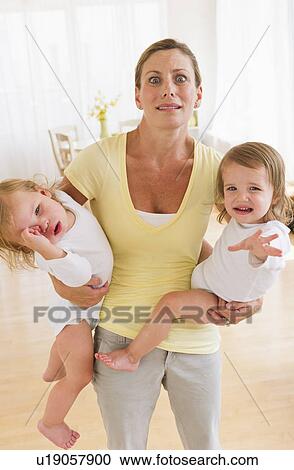 Stock Image - Mother holding crying daughters (2-3) and making facial expression. Fotosearch