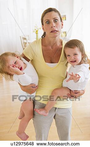 Mother holding crying daughters (2-3) and making facial expression View Large Photo Image Stock Photo - Mother holding crying daughters (2-3) and making facial expression. Fotosearch