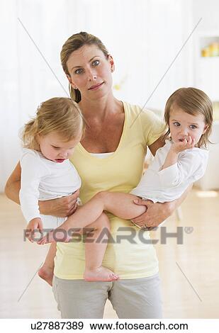 Stock Photo - Mother holding daughters (2-3) and making facial expression. Fotosearch