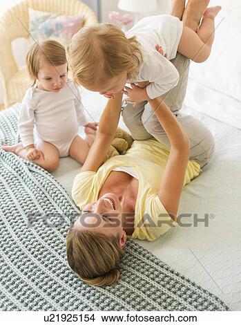 Picture - Mother playing with daughters (2-3) on bed. Fotosearch