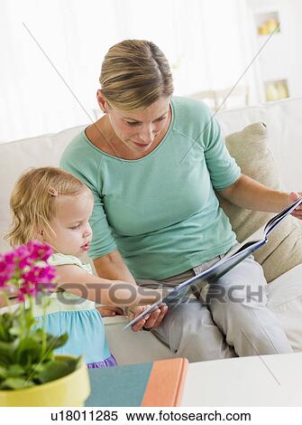 Stock Photography - Mother with daughter (2-3) reading book on sofa. Fotosearch