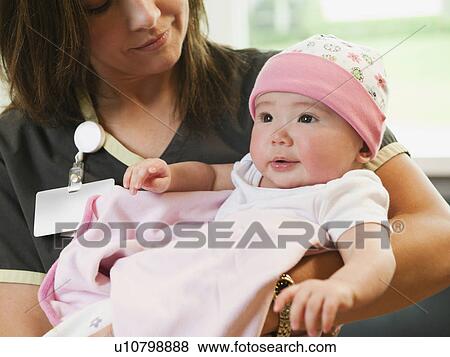 Stock Photo - Nurse holding baby girl (2-5 months). Fotosearch