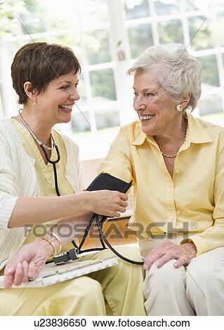 Stock Image - Nurse taking pulse of senior woman in nursing home. Fotosearch