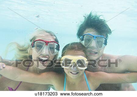 Stock Image - Parents with daughter (10-11) swimming underwater. Fotosearch