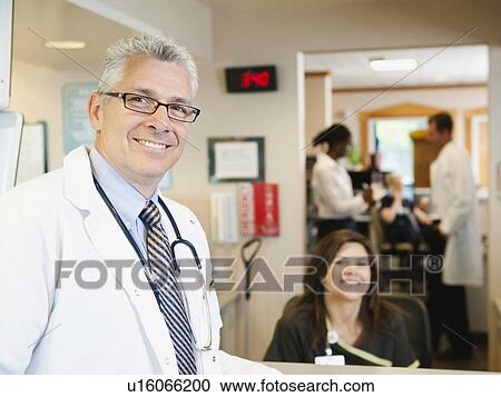 Stock Image - Portrait of confident doctor with female nurse in background. Fotosearch