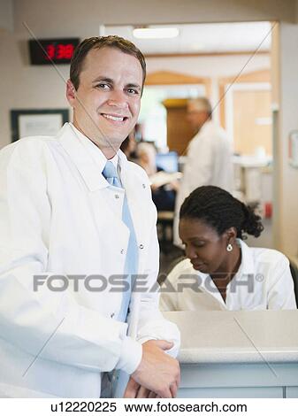 Stock Photography - Portrait of doctor with hospital receptionist working in background. Fotosearch