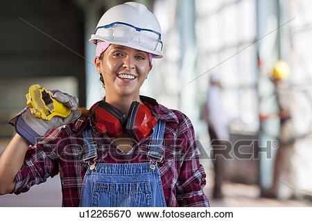 Stock Image - Portrait of female manual worker wearing hardhat. Fotosearch